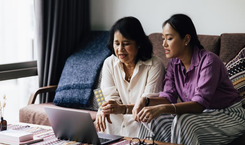 Older mother looking at pills with daughter at coffee table
